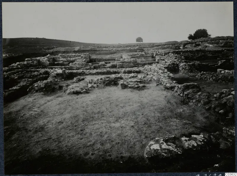 Stone wall foundations of Soli's Cholades temples across a cleared excavation area, with a low hill behind