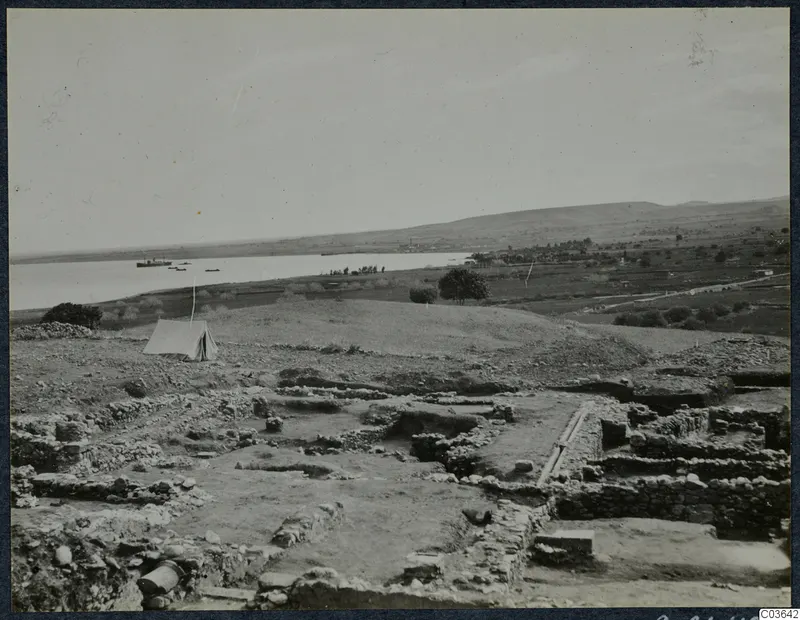 Excavated stone wall foundations at Soli, with a canvas tent on the left and the sea and boats beyond