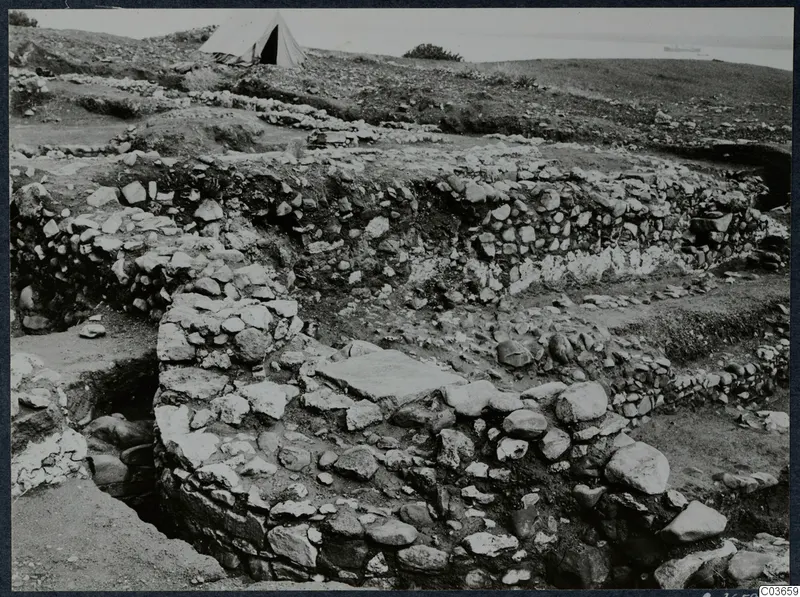 Excavated stone walls at Soli, Cholades, with a white tent on the hill and the sea beyond