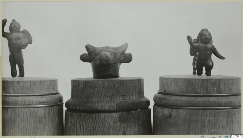 Three small bronze figurines on wooden stands: two standing human figures and an animal head with horns.