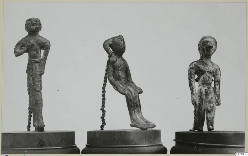 Three small bronze figurines on wooden bases: two standing figures and one seated figure leaning to the side