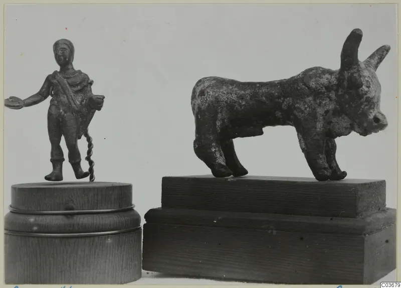 Two small bronze figures on wooden bases: a standing human figure holding a dish, and a horned bronze bull.