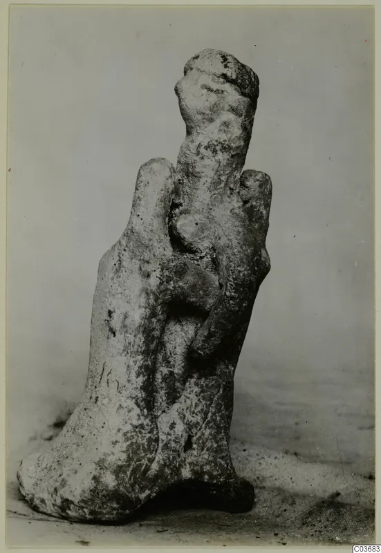 Terracotta figurine of a standing human figure with a rounded head, photographed on a grey surface