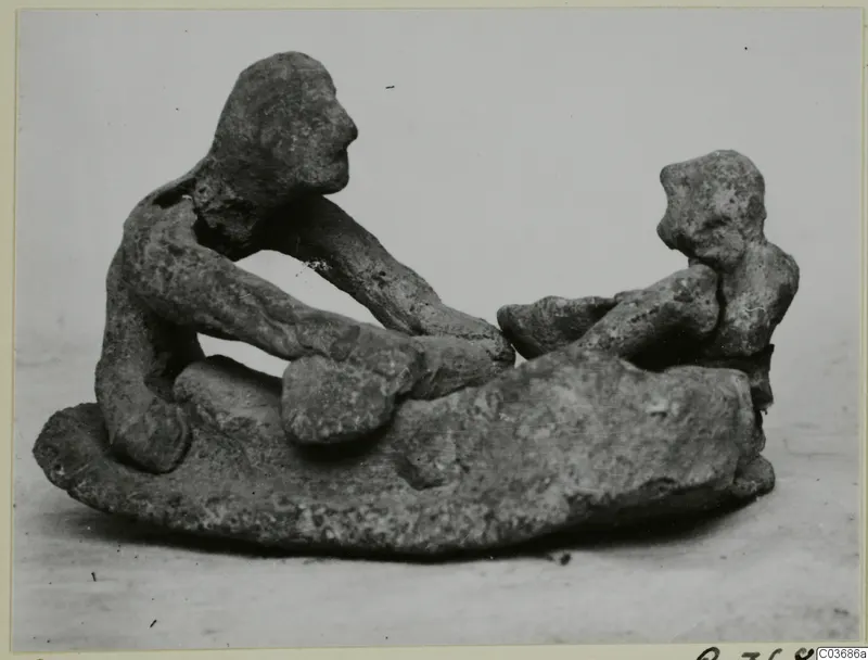 Terracotta figurine group of two figures on a rounded base, one seated and reaching toward the other