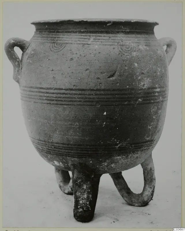 Pottery vessel with two loop handles and three tubular legs, decorated with dark painted bands and concentric circles.
