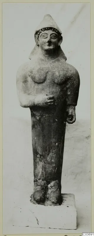 Terracotta figure with a tall conical cap and beaded headband, standing on a rectangular plinth.