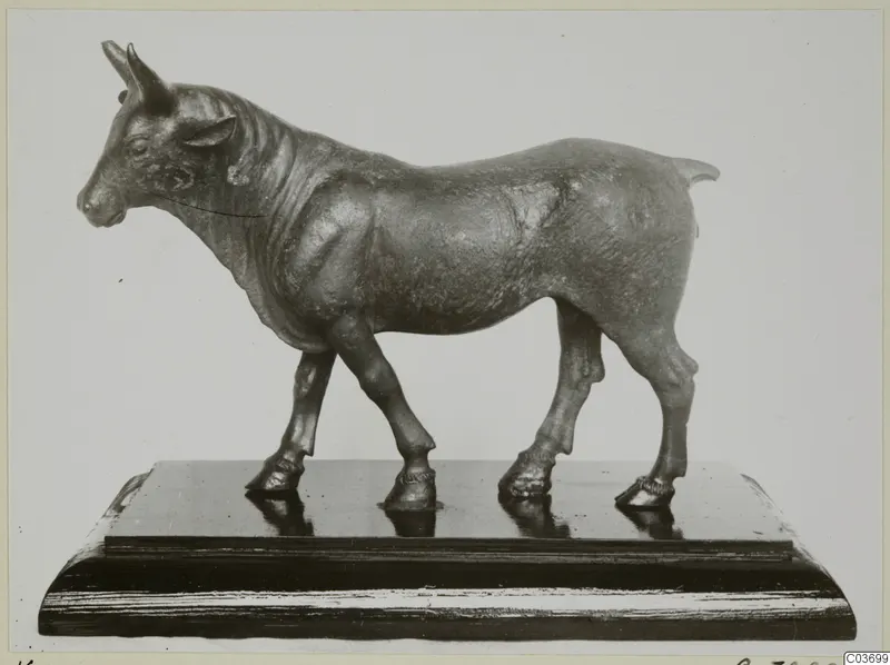 Bronze statuette of a standing bull facing left, mounted on a dark wooden base.