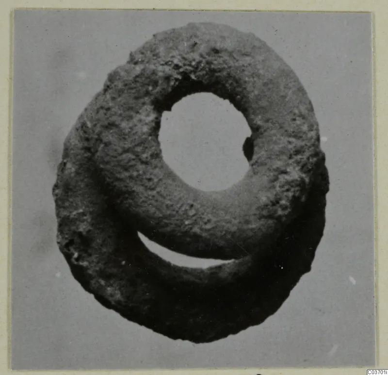 Silver object from Vouni: a ring-shaped find with a large central hole and a rough, dark, corroded surface.