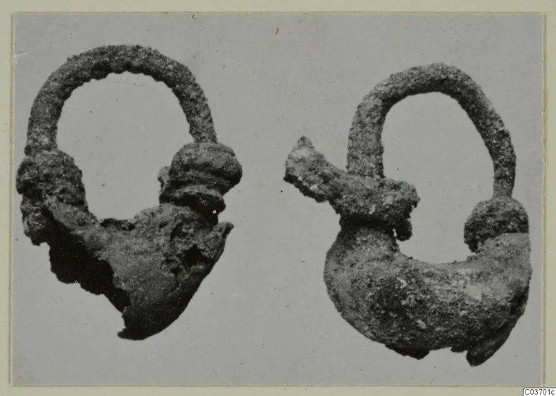 Two corroded metal objects with arched loops, from Vouni T. 1-16