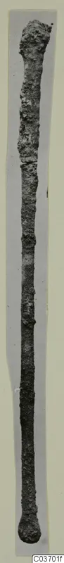 Long corroded bronze implement with a swollen top end and rounded knob at the bottom, from Vouni.