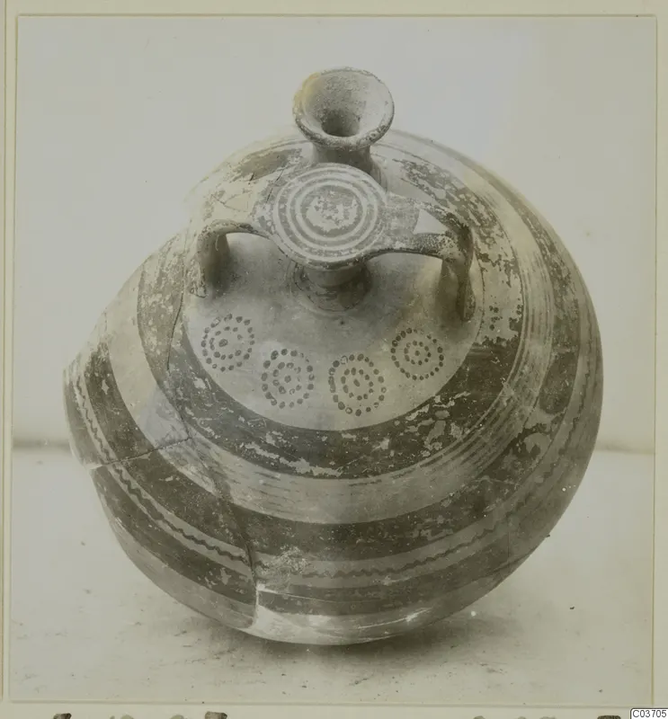 Round-bodied pottery vessel with a tall neck, two handles and painted bands and concentric circle motifs, photographed on a plain surface.