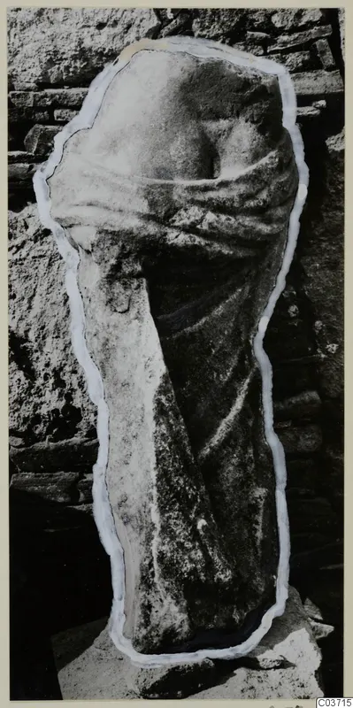 Back view of a draped marble statue fragment from Galini, standing against a stone wall
