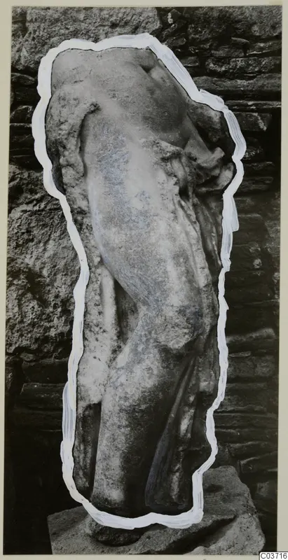 Marble sculpture fragment of a headless standing figure on a stone base, against a stone wall