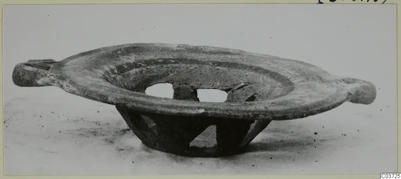 Shallow pottery bowl with two projecting lug handles, standing on a perforated openwork base, seen from the side