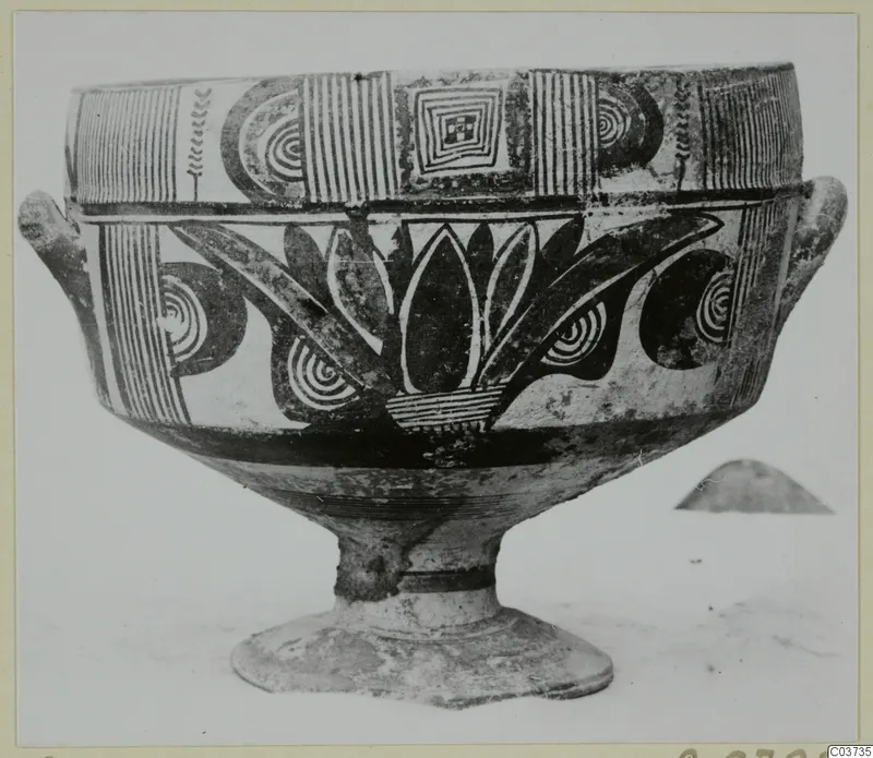 Footed pottery vessel with two side lugs and black painted bands, spirals and leaf-like motifs on a pale ground