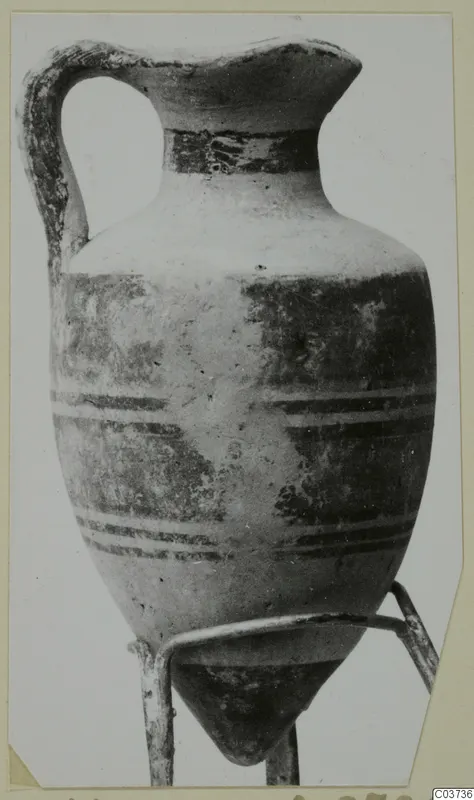 Jug with a single strap handle and dark painted horizontal bands, shown on a thin wire stand.
