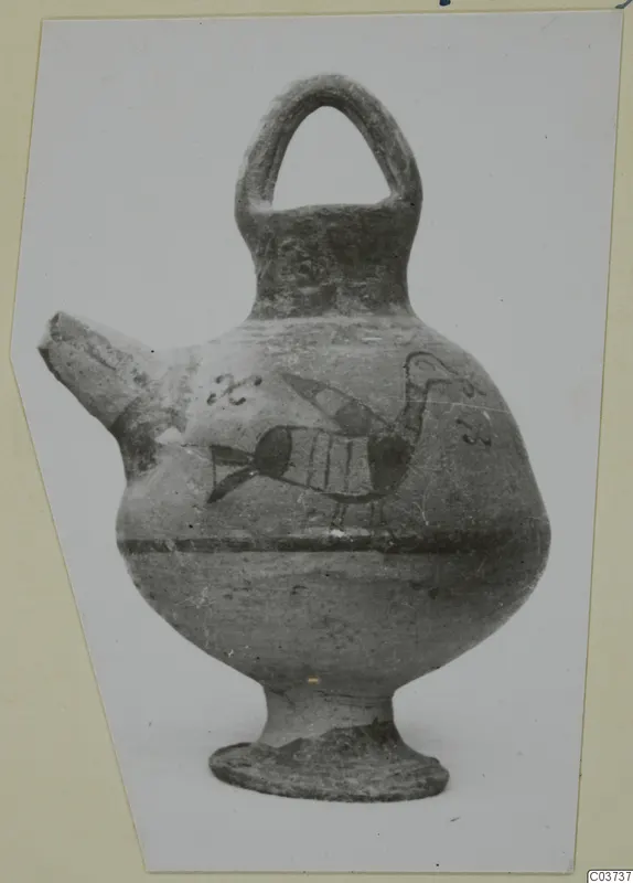Painted pottery vessel with a strap handle and a broken spout, with a bird-like motif on the body, photographed on a card mount