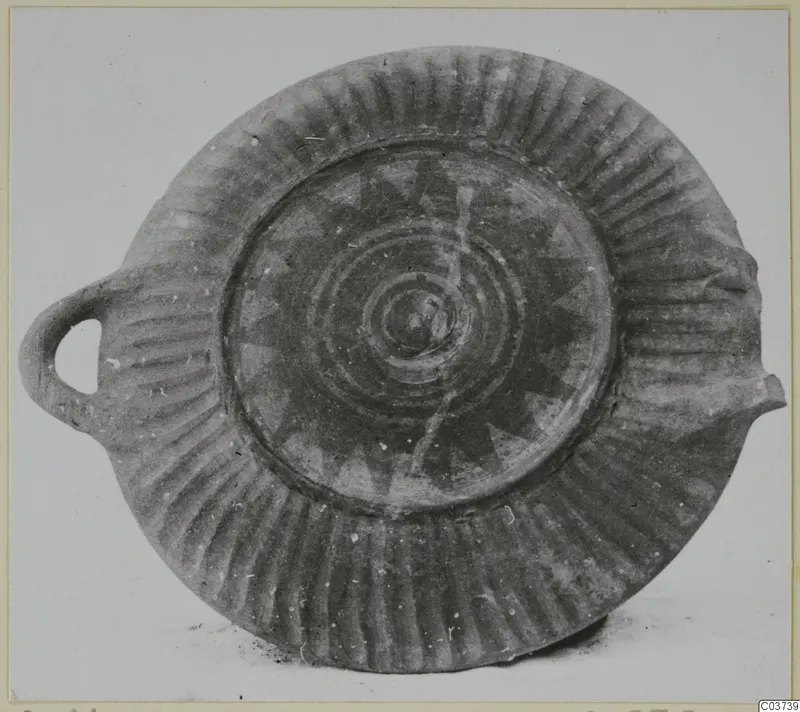 Shallow pottery dish with a loop handle, radial fluting on the rim and a painted star and concentric circles in the centre