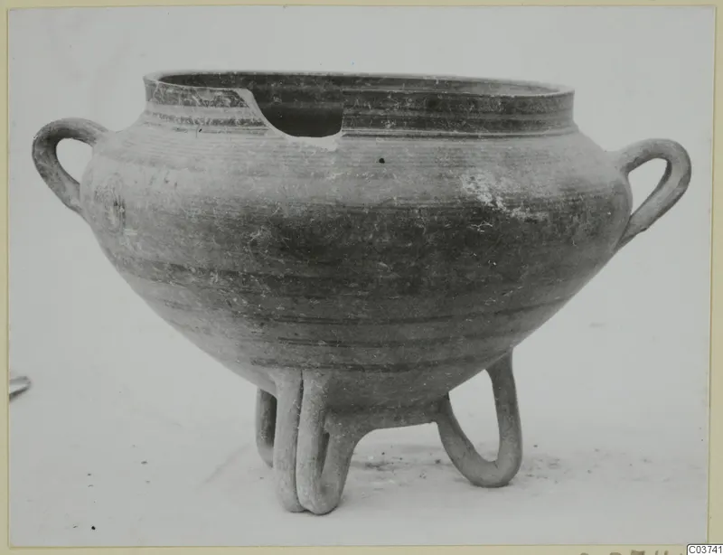 Round pottery vessel with two loop handles and three tubular feet, rim broken at the front