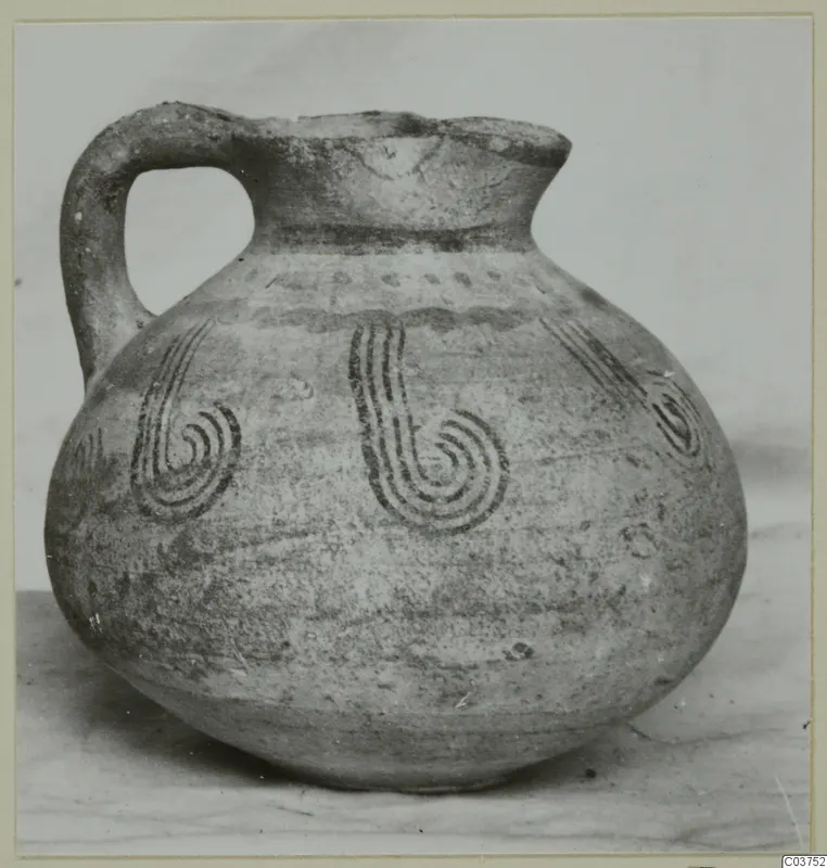 Round-bellied jug with a loop handle and dark spiral motifs painted on its body.
