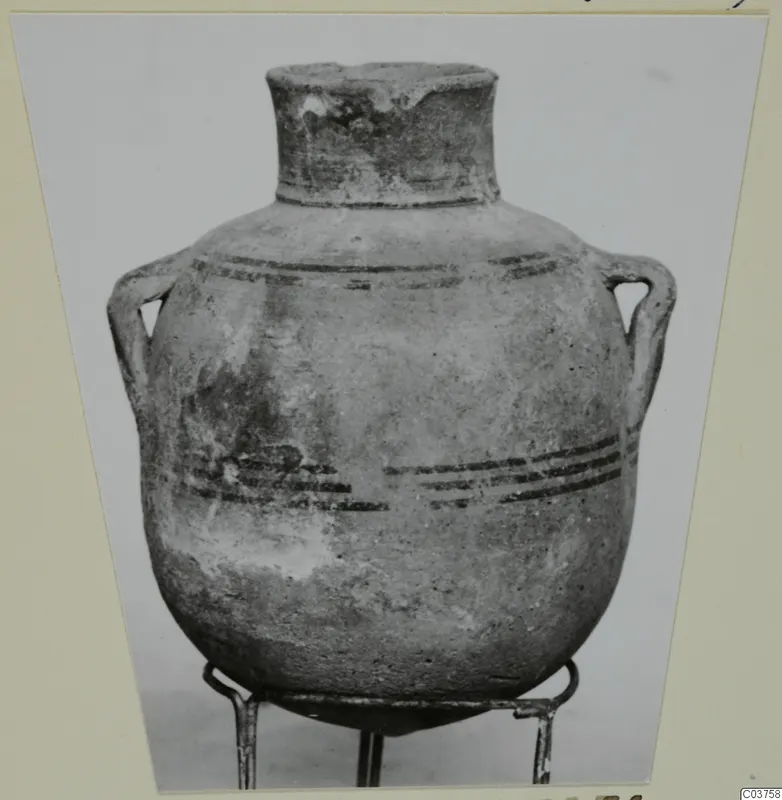 Globular two-handled pot with a short neck and dark painted horizontal bands, shown on a metal stand