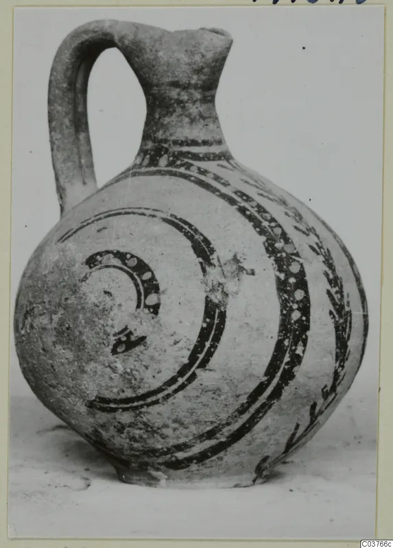 Painted pottery jug with a strap handle, dark bands and spirals with white dots on a pale body