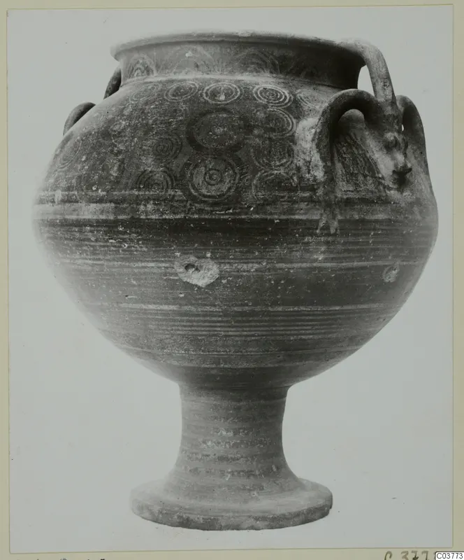 Pottery vessel on a tall ringed stem foot, with concentric circle motifs and a head-shaped handle attachment
