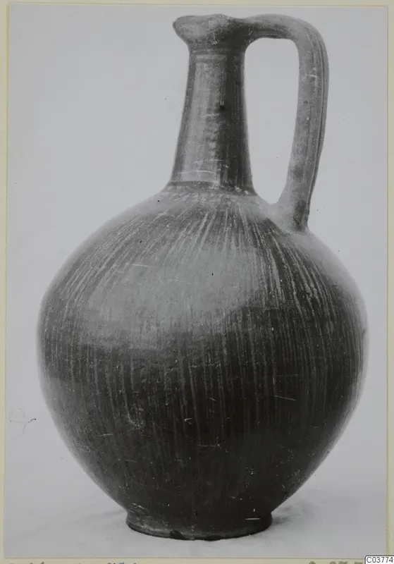 Black-burnished jug with a tall neck, single strap handle and stroke-polished surface, photographed against a plain background.