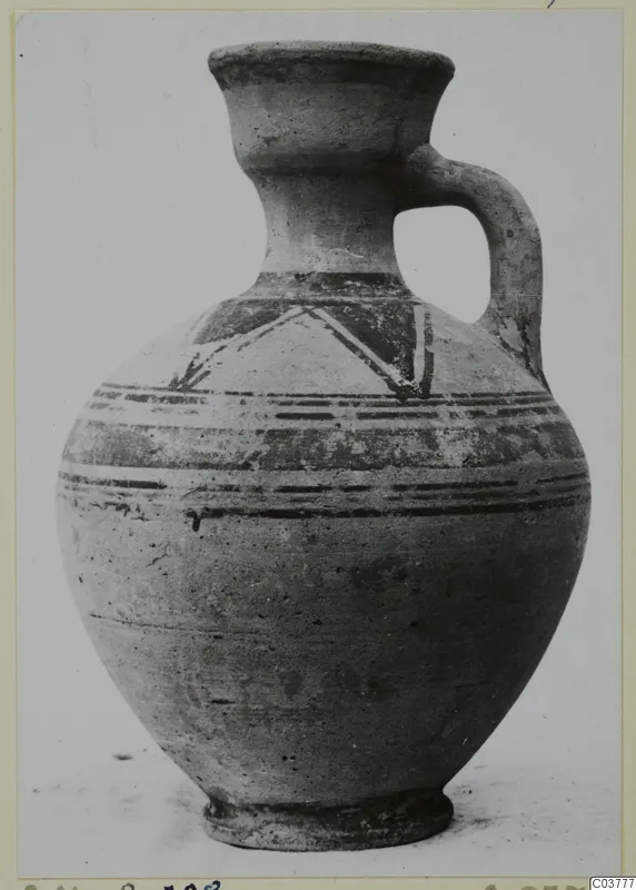 Painted jug with a high collar neck, one loop handle and bands of dark paint with a zigzag motif on the shoulder.