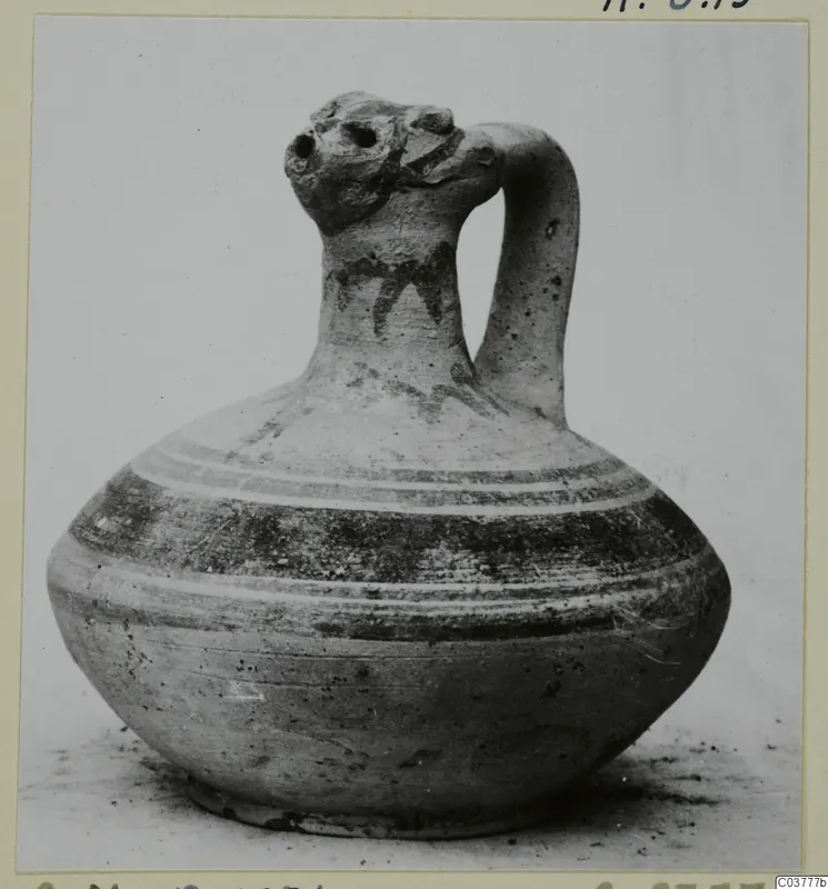 Pottery jug with a rounded body, strap handle and dark painted bands, shown on a plain background