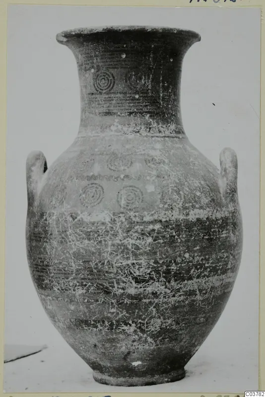 Pottery vessel with two handles and concentric circle motifs, photographed upright on a pale surface, Black-on-Red I-III.