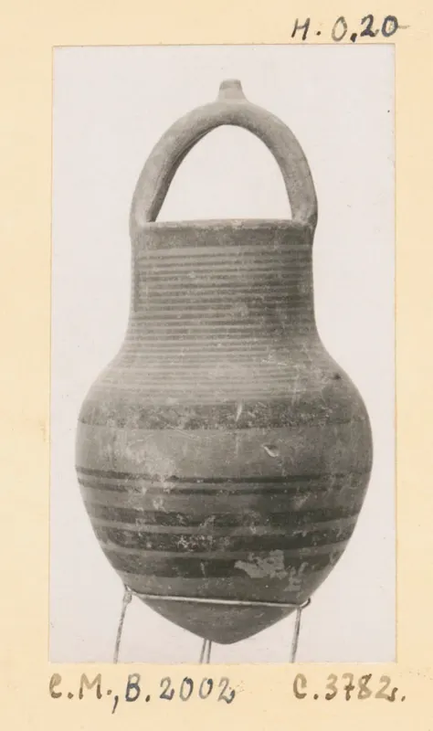 Black-on-Red pottery jug with a loop handle, ribbed neck and dark painted bands, photographed on a wire stand