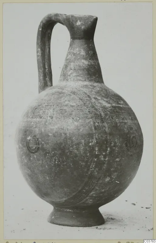 Painted pottery jug with a tall neck, strap handle and round body, standing on a ring foot