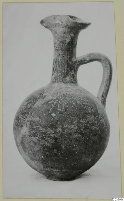 Round-bodied jug with a tall narrow neck, flared lip and strap handle, photographed against a pale background
