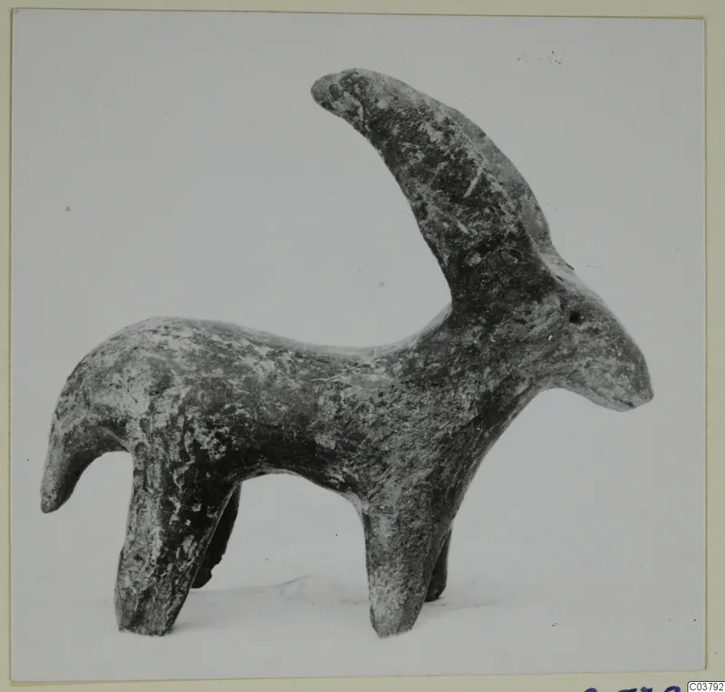 Small figurine of a horned animal standing on four legs, with a long curved horn and a mottled dark surface.