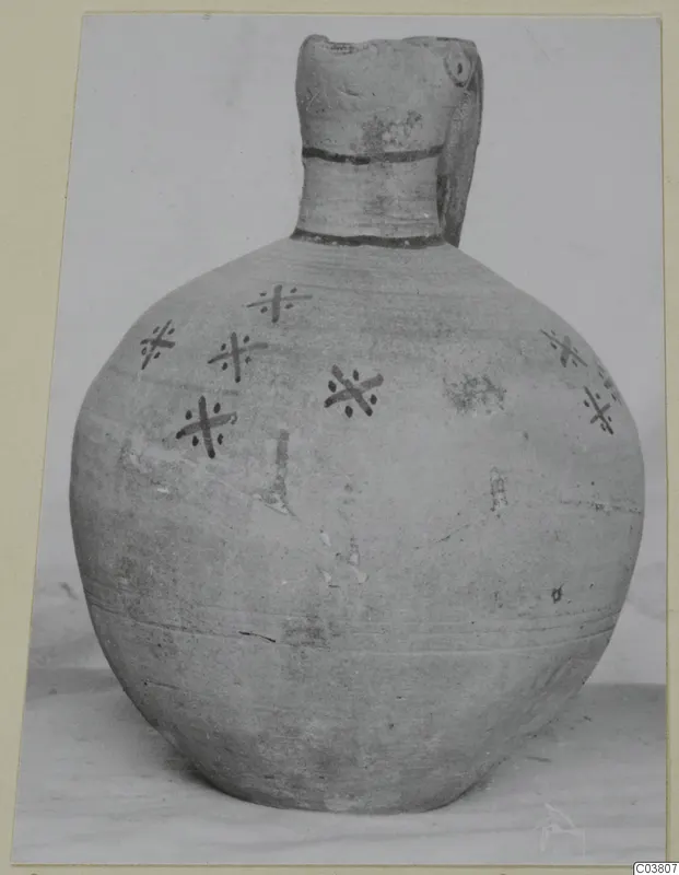 Round-bodied jug with a tall neck and dark cross-shaped painted motifs with dots on its shoulder and body