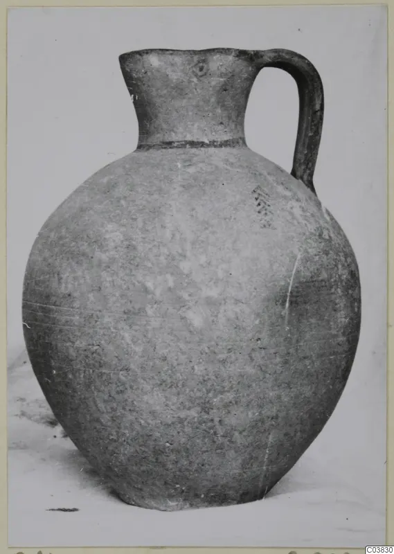 Round-bodied jug with a tall flared neck and a single strap handle, photographed against a plain background.