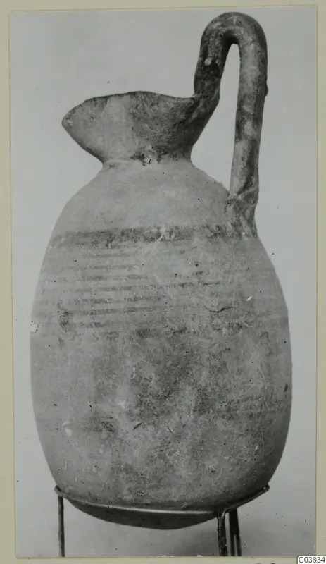 Pottery jug with a tall strap handle and dark painted horizontal bands on the body