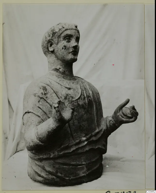 Sculpted bust of a figure with short hair and a draped garment, from Cyprus, one hand raised and one held out