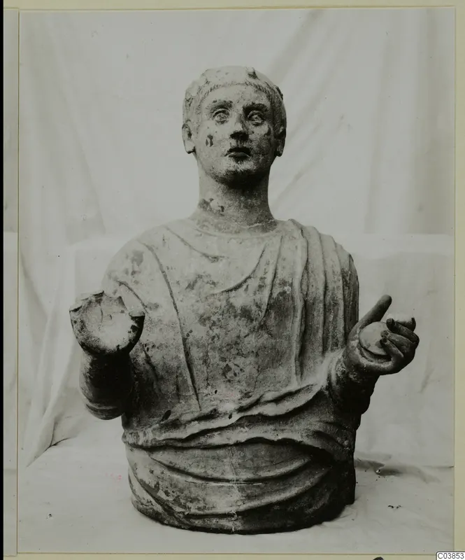 Stone bust of a draped figure with raised hands, photographed against a white cloth.