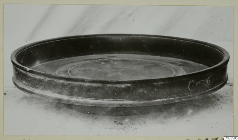 Shallow dark bowl with a spiral scroll motif on its outer wall, photographed on a pale surface
