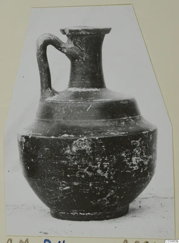 Dark glazed jug with a single loop handle and a flared rim, photographed against a pale backdrop.