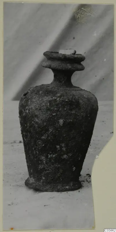 Bronze pot, heavily corroded, with a stepped collar rim, narrow neck and footed base
