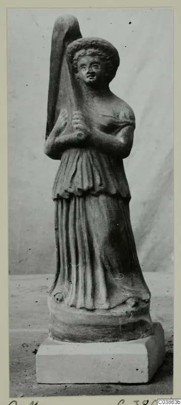 Terracotta figurine of a standing female figure with curly hair, holding a tall object, on a rectangular plinth