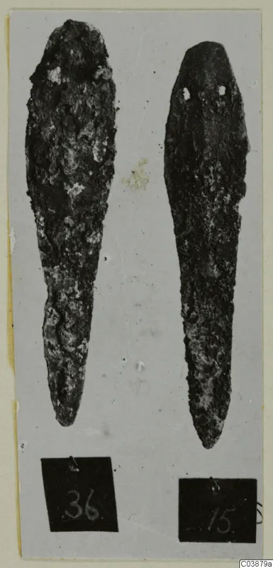Two corroded metal tools lying side by side on a grey card, with number labels below them.
