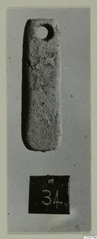 Small elongated pierced pendant, photographed upright on grey card with a number label, from Ayios Iakovos