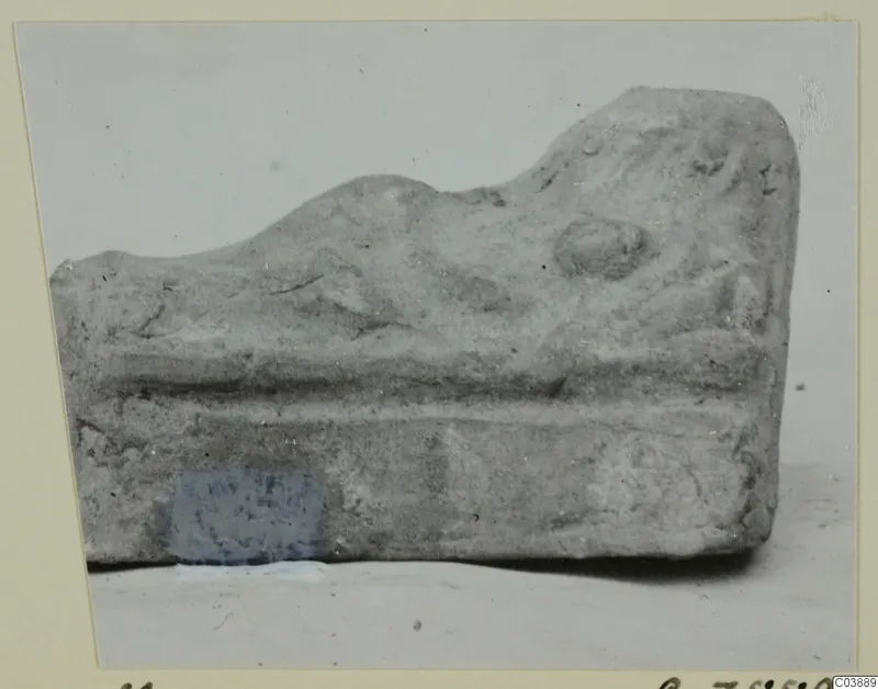Fragment of a terracotta minor plastic object with a raised ridge and a rounded knob, photographed side-on.