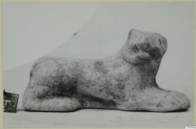 Small terracotta figurine of a crouching animal with its head raised, photographed on a pale background
