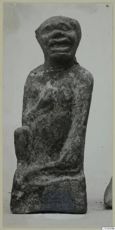 Small seated figure with a rounded head, wide open mouth and a chipped neck, photographed against a pale background.