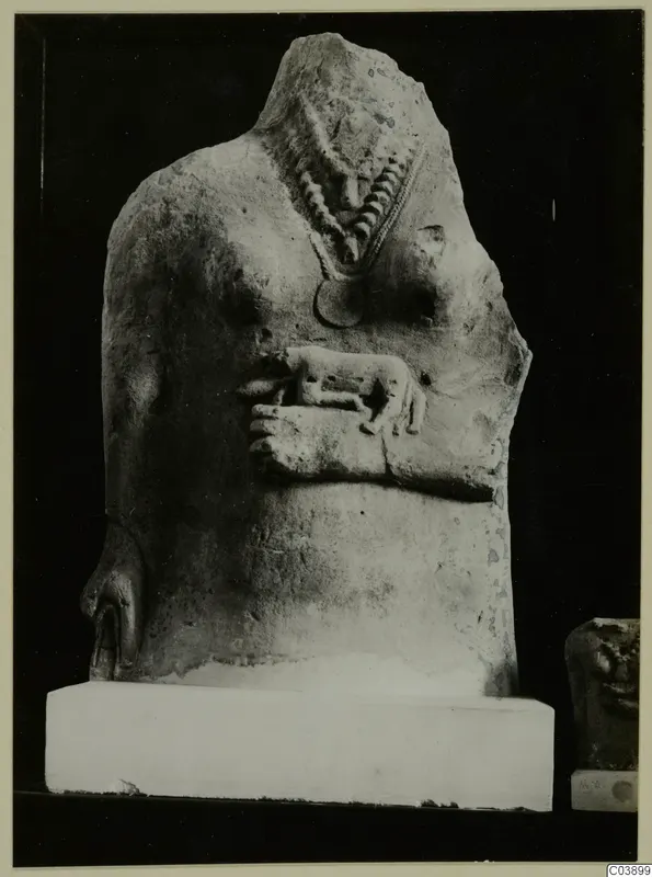 Headless limestone statue torso with a bead necklace, a round pendant and a small animal in relief on the chest
